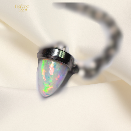 Close-up van de synthetische opaalhanger van de Opal Ear Threader. De steen toont een iriserende kleurreflectie in tinten blauw, roze en groen, met een glanzende afwerking in chirurgisch staal. Luxe en elegant detailshot.