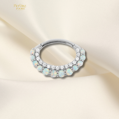 Zilverkleurige click ring van cobalt chromium staal met zirconia en opaalsteentjes. Luxe ovale piercing met scharniersluiting.