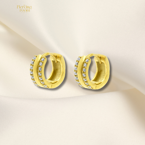 Goudkleurige chirurgisch stalen huggie hoops met dubbele rij zirconia’s. Luxe click oorringen met glanzende afwerking.