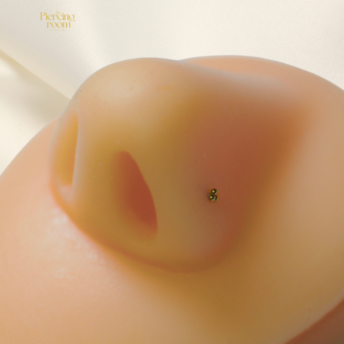 Triple Bead Nose Stud van titanium met gouden P.V.D. coating, gedragen in de neus. Drie bolletjes voor een subtiele en speelse look.