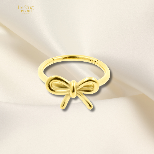 Gouden conch clicker piercing met strikdetail, gemaakt van nikkelvrij chirurgisch staal. Elegant design, eenvoudig open en dicht te klikken.