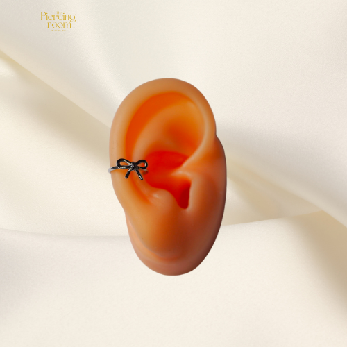 Zilveren conch clicker met strikdesign, gedragen in het oor. Gemaakt van nikkelvrij chirurgisch staal. Perfect voor conch en helix piercings.